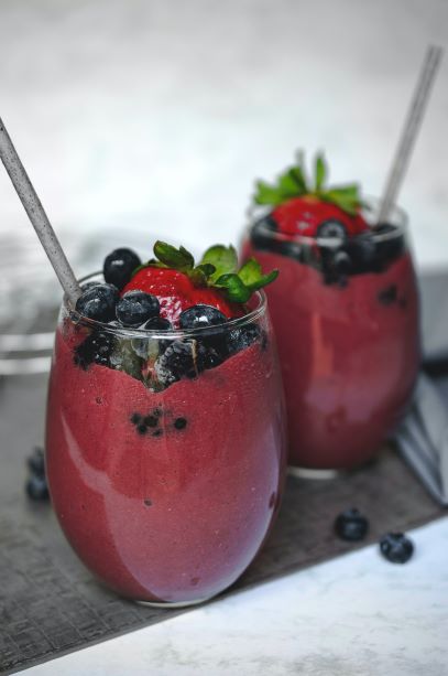 Two berry smoothies in a short wine glass with straw blueberries, blackberries and strawberries on top.