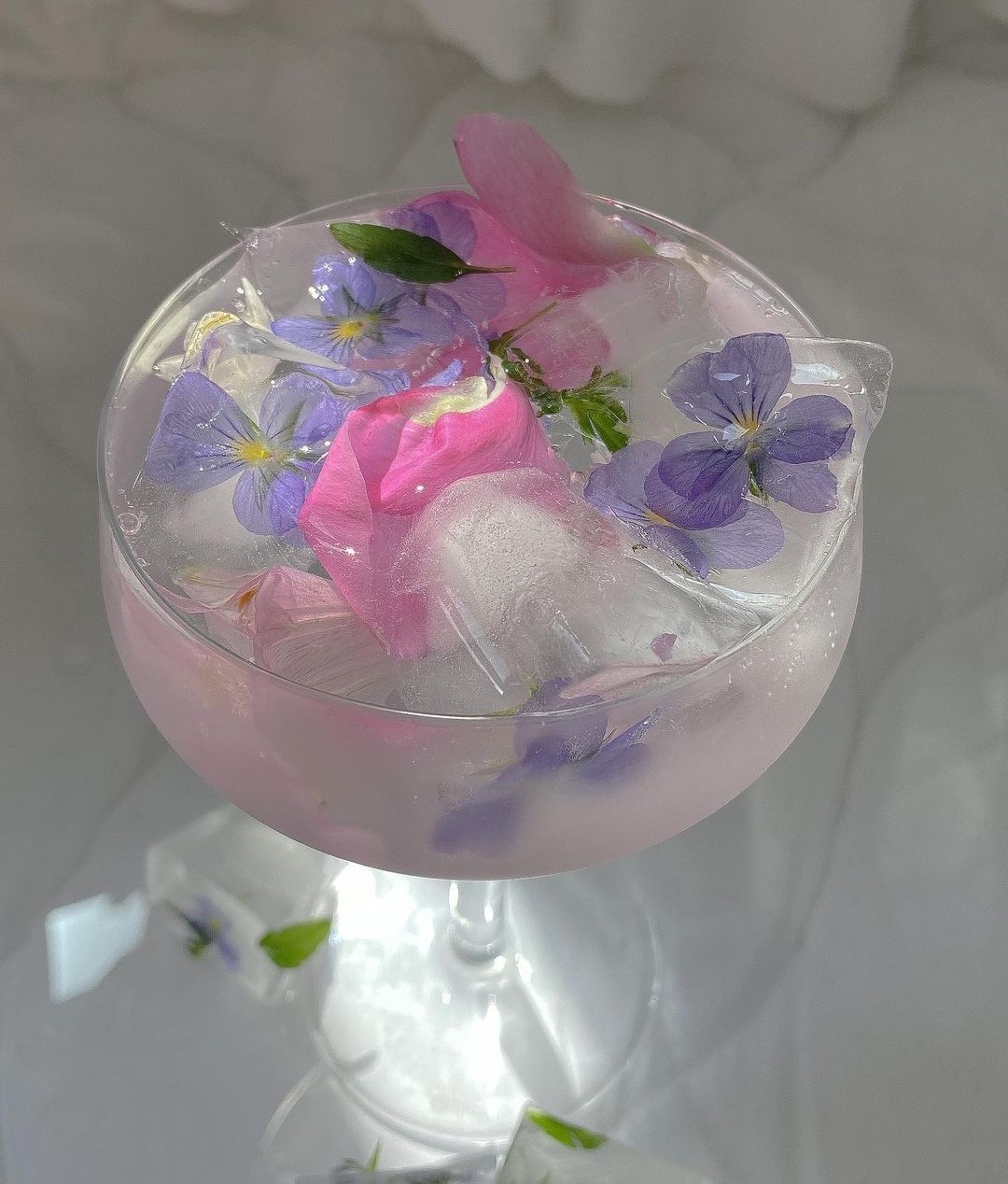 champagne coupe with ice water and pink and purple flowers.